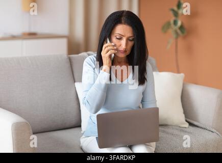 Seriöse ältere Frau im Gespräch auf dem Smartphone mit Laptop Stockfoto
