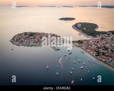 Luftbild des Sonnenuntergangs über die Halbinsel der Altstadt von Primosten und der Bucht mit Segelbooten, die in der Adria in Kroatien vor Anker liegen Stockfoto