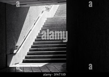 Dramatische Schwarz-Weiß-Treppe, die von einem dunklen unterirdischen Gang ins helle Tageslicht führt Stockfoto