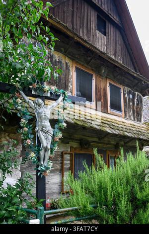 Ein Kruzifix im Vorgarten eines traditionellen Holzhauses im Dorf Cigoc. Lonjsko Polje Naturpark, Kroatien. Stockfoto