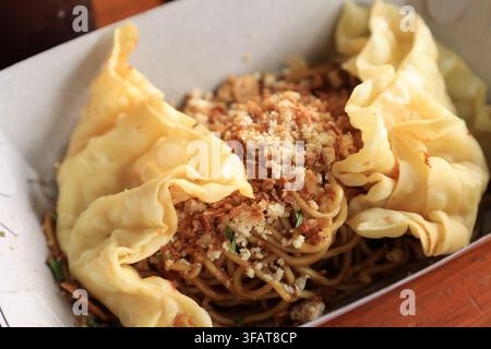 Nahaufnahme Mie Gacoan, beliebte scharfe indonesische Nudeln mit gebratenem Knödel, serviert auf einem Pappteller zum Mitnehmen Stockfoto