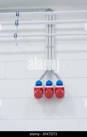 Kommerzielle elektrische Installation mit starren Leitungsrohren und dreiphasigen Industrie Steckdosen an einer weißen Wand Stockfoto