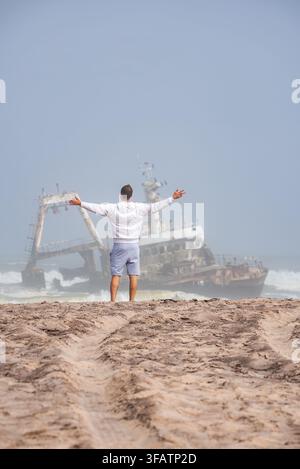 Mann steht am sandigen Ufer und betrachtet das Wrack von Zeila in Namibia Stockfoto