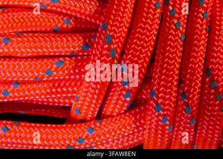 Dichte Makroaufnahme von sich überlappenden und verflochtenen orangefarbenen Paracord, die eine lebendige abstrakte Seiltextur erzeugen Stockfoto