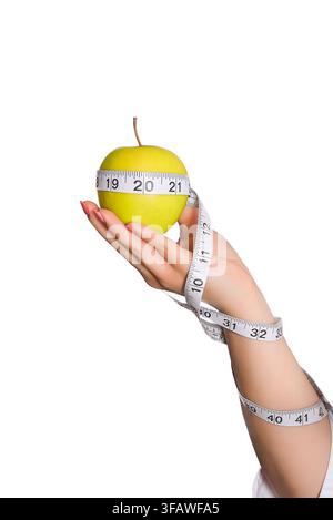 Hand, die einen kleinen grünen Apfel hält, der mit einem Maßband umwickelt ist, vor einem sauberen weißen Hintergrund, gesundes Ernährungs-Konzept. Stockfoto