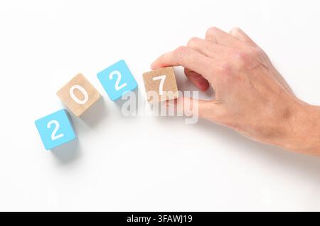 Eine Hand arrangiert hellblaue und hölzerne Würfel mit den weißen Zahlen auf weißem Hintergrund und Kopierraum. Stockfoto
