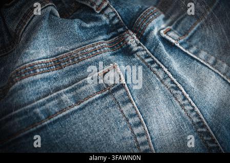 Detaillierte Nahaufnahme von blauem Denimjeans-Stoff mit klassischer orangefarbener Naht und Säumen. Stockfoto