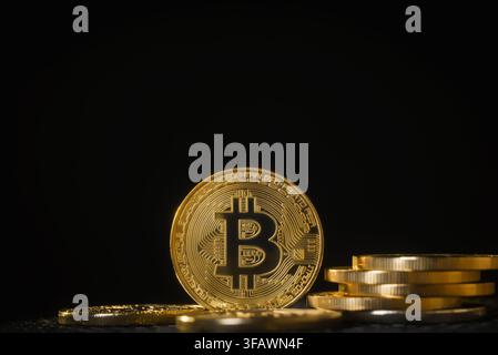 Bitcoin-Kryptowährungsmünze aufrecht auf einer reflektierenden Oberfläche mit einem Stapel Münzen und warmem Licht auf dunklem Hintergrund. Stockfoto