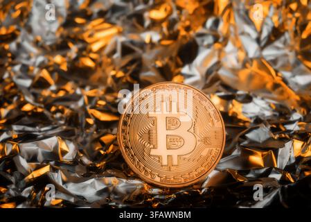 Bitcoin-Kryptowährungsmünze steht auf einem reflektierenden goldenen Folienhintergrund und symbolisiert Luxus, Reichtum und Erfolg. Stockfoto