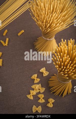 Oberblick von oben auf ein rohes, trockenes Spaghetti-Bündel mit verstreuten Farfalle-Nudelteilen auf einem dunklen Hintergrund, beim Kochen. Stockfoto
