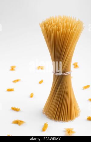 Vertikales Bündel roher trockener Spaghetti-Pasta, aufrecht stehend auf einem sauberen weißen Hintergrund, italienische Küchenzutat. Stockfoto