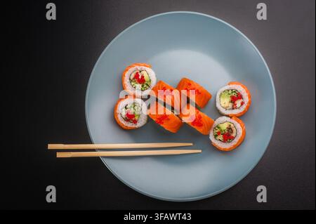 Frisches japanisches Sushi-Set mit Lachs und Frischkäse, serviert auf einem hellblauen Teller mit hölzernen Essstäbchen, Nahaufnahme. Stockfoto