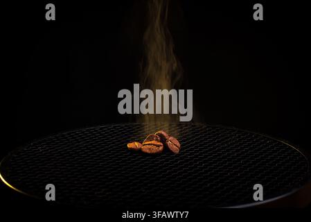 Kleine Gruppe von gerösteten Kaffeebohnen im Rauch auf einer dunklen Oberfläche Stockfoto