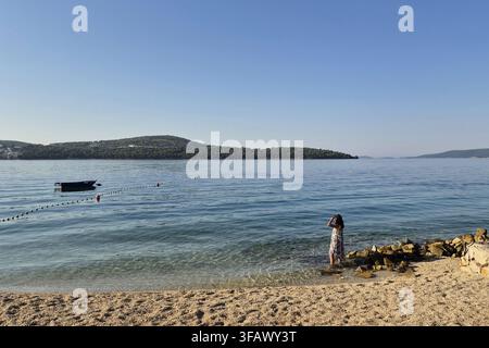 Weite Landschaftsansicht einer friedlichen Bucht an der Adria mit einem kleinen Boot, das in ruhigem Wasser vor Anker liegt, und einer Person, die nahe der felsigen Küste steht. Stockfoto