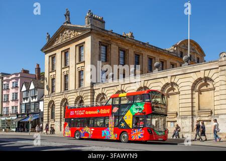 Red City Sightseeing Open-Top-Doppeldecker-Hop-On-Hop-Off-Tourbus fährt an historischen Universitätsgebäuden in Oxford, Oxfordshire, England, vorbei. Stockfoto