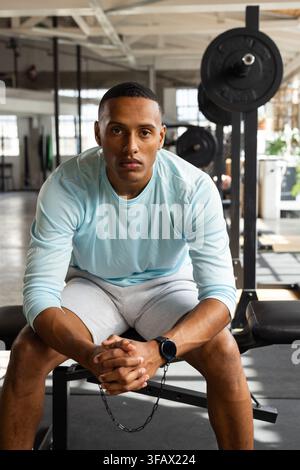 Afroamerikanischer Erwachsener sitzt auf einer Hantelbank und ruht sich zwischen Sätzen mit einer belasteten Stange aus Stockfoto