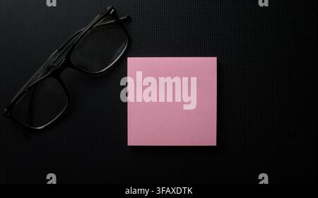 Rosa Haftnotiz und Brille auf dunklem strukturiertem Hintergrund Stockfoto