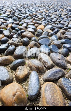 Traditioneller italienischer Mosaikbelag aus glatten, abgerundeten Flusskieseln in Schattierungen von dunklem Grau, glänzendem Schwarz und erdigem Braun. Stockfoto
