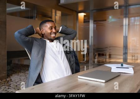 Lächelnder afrikanischer Geschäftsmann am Ende des Arbeitstages, zurückgelehnt im Stuhl Stockfoto
