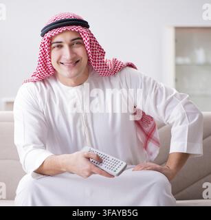 Der junge arabische Mann schaut fern und sitzt auf dem Sofa Stockfoto