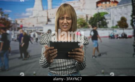Frau, die Tablette mit beiden Händen hält, grimmig beim Lesen auf einer belebten Straße; Frustrationskonzentration. Stockfoto