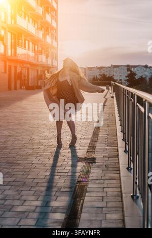 Frau tanzt bei Sonnenuntergang, dreht sich auf einem Stadtweg zur Goldenen Stunde und drückt Freiheit und Freude in der städtischen Umgebung aus Stockfoto