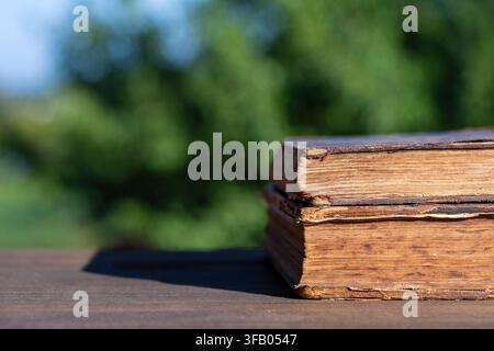 Stapel alter Vintage-Bücher auf Holztable im Freien. Nahaufnahme von zwei gealterten antiken Büchern mit abgenutzten Ledereinbänden, gestapelt auf Holzoberfläche vor Stockfoto