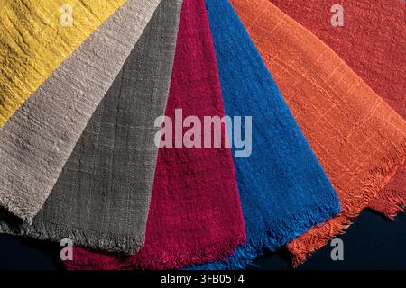 Oberansicht von mehrfarbigen Leinen-Textilstoffmustern, die fächerförmig angeordnet sind und natürliche Textur und gefranste Kanten zeigen, Nahaufnahme. Ideal für Innenarchitektur Stockfoto