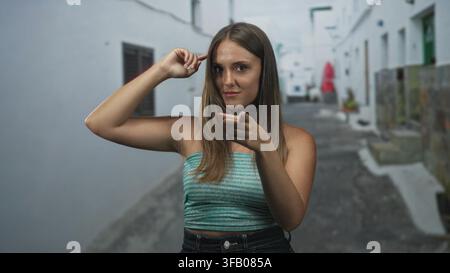 Junge Frau zeigt mit dem Finger auf den Betrachter und tippt mit dem Zeigefinger an die Schläfe auf der Straße, trägt ein türkisfarbenes Tube-Top und Jeans; selbstbewusstes Denken. Stockfoto