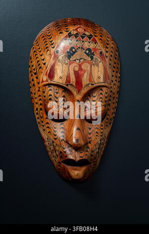 Handgefertigte afrikanische Holzmaske auf schwarzem Hintergrund. Frontansicht Nahaufnahme einer dekorativen handgeschnitzten Holztribalmaske mit aufwendiger schwarzer und r Stockfoto