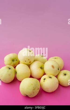Vertikale Hochwinkelaufnahme von hausgemachten weißen transparenten Äpfeln, die auf einem hellrosa Hintergrund gestapelt sind, süße Bio-Gartenfrüchte Sommerernte-Arrangement Stockfoto