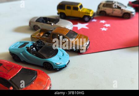 Abgenutzte Metallspielzeugautos auf rotem Papier mit weißen Sternen aufgereiht, vorne ein blauer Sportwagen und ein abgewetzter orangefarbener Pickup sowie dahinter ein silberner Cabriolet, die gezeigt werden Stockfoto