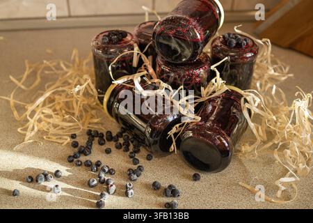 Hausgemachte Wildwald-Heidelbeer-Marmelade in kleinen Gläsern auf rustikaler Tischoberfläche, umgeben von frischen rohen Beeren und dekorativen Holzspänen Stockfoto