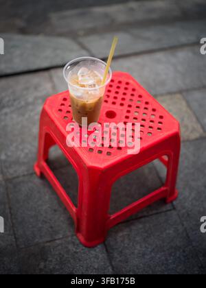 Vietnamesischer Eiskaffee cà phê sữa đá in einem Plastikbecher auf einem roten Plastikhocker auf dem Bürgersteig, Ho-Chi-Minh-Stadt, Vietnam Stockfoto