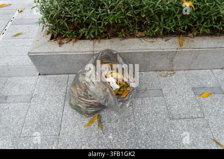 Plastiktüte gefüllt mit Müll auf gepflasterter Straße. Stockfoto