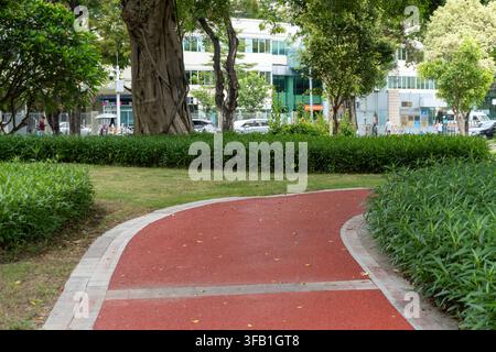 Kurviger roter Weg durch einen städtischen Park mit Grünflächen. Stockfoto