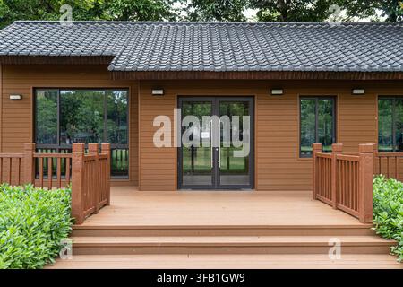 Holzhausfassade mit Terrasse in einem üppigen Garten. Stockfoto