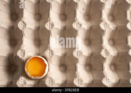 Oberansicht eines weißen rissigen Eies mit Eigelb in einer Kartonschale Stockfoto
