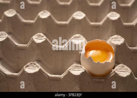Oberansicht eines weißen rissigen Eies mit Eigelb in einer Kartonschale Stockfoto
