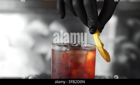 Barkeeper garniert Cocktail mit Orangenschale, bereitet erfrischendes Getränk auf der Theke zu, professioneller Mixologie-Service Stockfoto