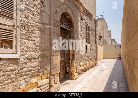 Kairo, Ägypten, 26.07.21. Vernachlässigtes altes Gebäude mit Holztüren und Fensterläden in der engen Steinrinne im koptischen Kairo, Ägypten. Stockfoto