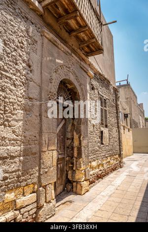 Vernachlässigtes altes Gebäude mit Holztüren und Fensterläden, Steinmauer verziert mit religiösen Symbolen, Koptisches Kairo, Ägypten. Stockfoto