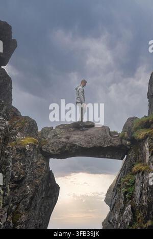 Ein Mann steht auf der Djevelporten-Felsenbrücke in Lofoten, Norwegen Stockfoto