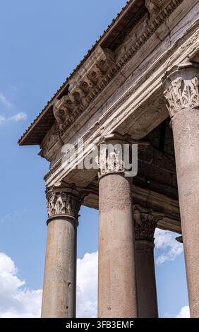 Niedrigwinkelaufnahme antiker römischer Tempelsäulen mit geschnitzten korinthischen Kapitellen und verwittertem Steinarchitrav unter einem klaren blauen Himmel in Rom, Italien Stockfoto