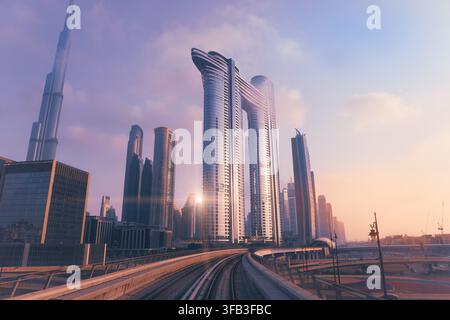 Panoramischer Blick auf das Geschäftsviertel von Dubai in den VAE mit dem Burj Khalifa, modernen Wolkenkratzern und geschwungenen Metrogleisen unter einem warmen Sonnenuntergang Stockfoto