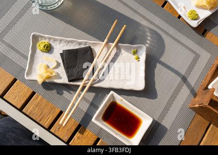 Oberflächennaher Nahaufnahme eines japanischen Sushi-Kondimenttabletts mit grünem Wasabi, eingelegtem Ingwer, Serviette und Sojasauce in weißen Keramikschalen auf einem gewebten Tischläufer Stockfoto