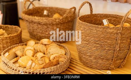 Frisches sortiertes Brot und Brötchen in rustikalen geflochtenen Körben auf dem Frühstücksbuffet eines Hotels, das eine warme und einladende Essensszene schafft. Stockfoto