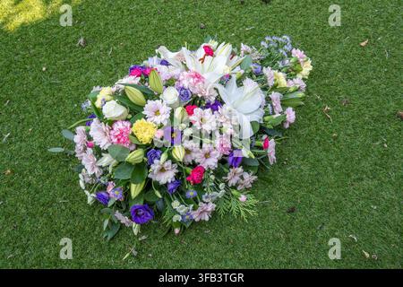 Eine Ansicht von oben eines bunten Beerdigungs-Kissenarrangements mit weißen Lilien, Rosen, Nelken und Chrysanthemen, das draußen ruhend platziert ist Stockfoto
