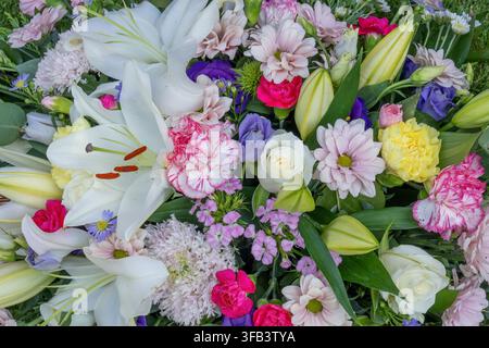 Eine detaillierte Vollbild-Aufnahme von oben eines Beerdigungsblumenarrangements mit auffälligen großen weißen Lilien, Rosen, Nelken und Tigergänseblümchen Stockfoto