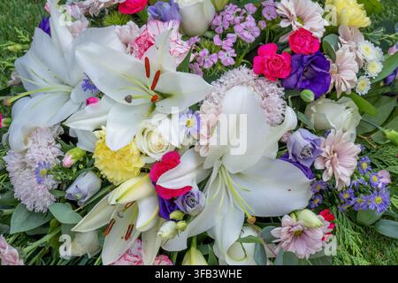 Eine detaillierte Vollbild-Aufnahme von oben eines Beerdigungsblumenarrangements mit auffälligen großen weißen Lilien, Rosen, Nelken und Tigergänseblümchen Stockfoto